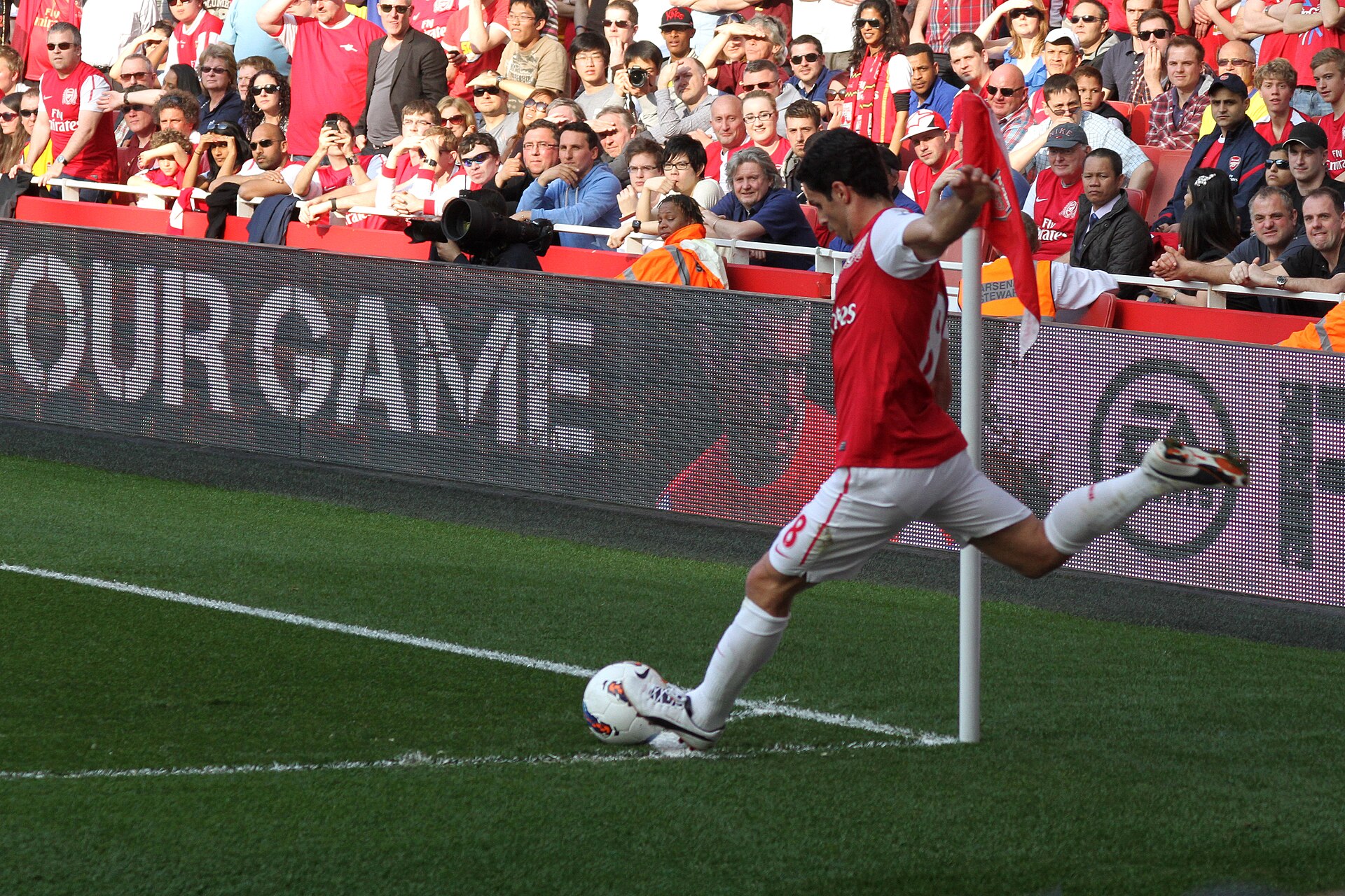 Mikel Arteta az Arsenal piros-fehér mezében szögletet rúg, a háttérben nézőkkel.