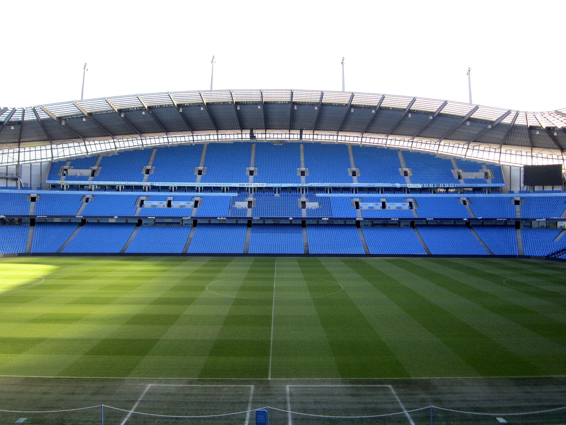 Az Etihad Stadion üres, kék lelátói és gondozott zöld futballpályája.